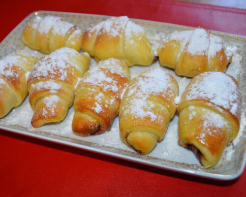 Plate of golden-brown croissants with powdered sugar on top