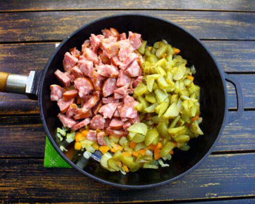 Добавляют в сковороду к зажарке огурцы и колбасу